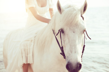 Girl in white dress with horse on the beach