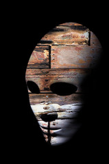 Textured mask with cracked rough wood  painted surface, neutral expression on dark background.