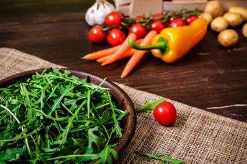 Arugula leaves in bowl. Fresh salad. Carrot, pepper and cherry tomatoes. Natural raw vegetables. Organic bio food on rustic wooden table.