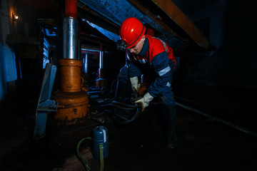 young miner man underground in a mine for coal mining in overalls is busy with work, repairing...
