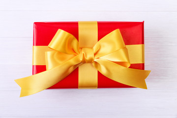 Gift box with yellow bow. Present wrapped with ribbon. Christmas or birthday red package. On white wooden table.