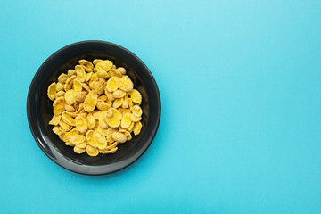 Yellow corn flakes in a black plate on a blue background. Place for the text.