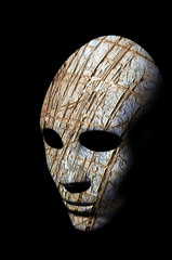 Textured mask with cracked rough wood  painted surface, neutral expression on dark background.
