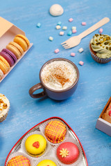 Cupcakes, macaroons and glazed donuts. Mug with whipped cream and cinnamon. Almond macaron cookies. Sweet dessert.