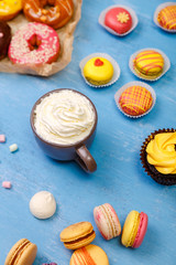 Macaroons, cupcakes and donuts. Mug with whipped cream. Almond macaron cookies with marshmallows. Sweet dessert.