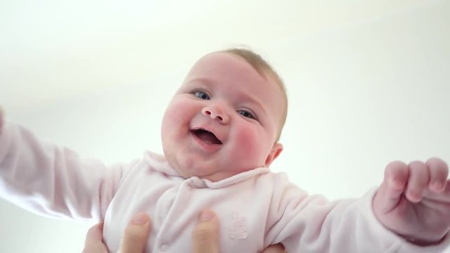 Happy flying little baby girl in pink suit in mother's hands.