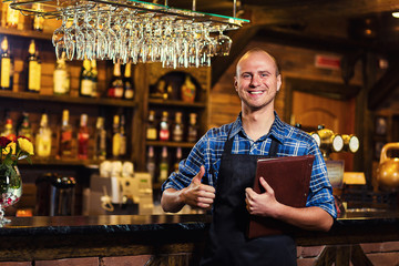 Barman at work in pub,Portrait of cheerful barman worker standing,Waiter giving menus,A pub.Bar.Restaurant.Classic.Evening.European restaurant.European bar.American restaurant.American bar.