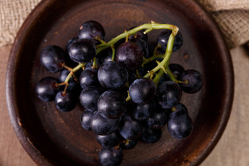 Dark grapes bunch. Ripe grape fruit on rustic plate. On wooden background.