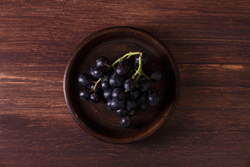 Dark grapes bunch. Ripe grape fruit on rustic plate. On wooden background.