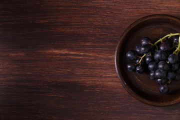 Dark grapes bunch. Ripe grape fruit on rustic plate. On wooden background.