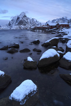 Snow capped rocks in the icy waters of Reine fishing village Bay, Lofoten Islands, Norway