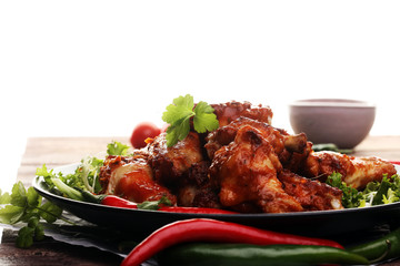 barbecue chicken wings close up on wooden tray with red spice sauce and salad