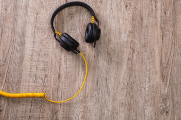 Headphones with yellow cable. Modern device for listening music. Sound earphones lying on wooden rustic background.