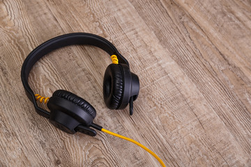 Headphones with yellow cable. Modern device for listening music. Sound earphones lying on wooden rustic background.