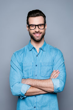 Portrait of happy fashionable handsome man in jeans shirt and glasses crossing hands and smiling
