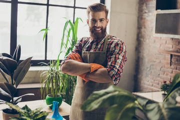 Portrait of young smiling gardener with crossed hands at the greenhouse looking after the flowers and plants