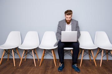 Portrait of young successful businessman sitting on a chair and working with laptop