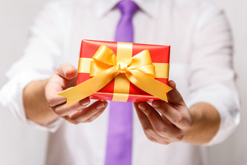 Male hands holding a gift box. Present wrapped with ribbon and bow. Christmas or birthday red package. Man in white shirt and necktie.