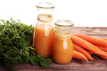 Fresh carrot juice in bottles and carrots on a grey wooden table