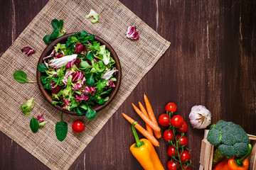 Provence salad. Leaves of endive or chicory, lamb and rose salad. Cherry tomatoes, pepper and carrot. Raw vegetables. On wooden table.