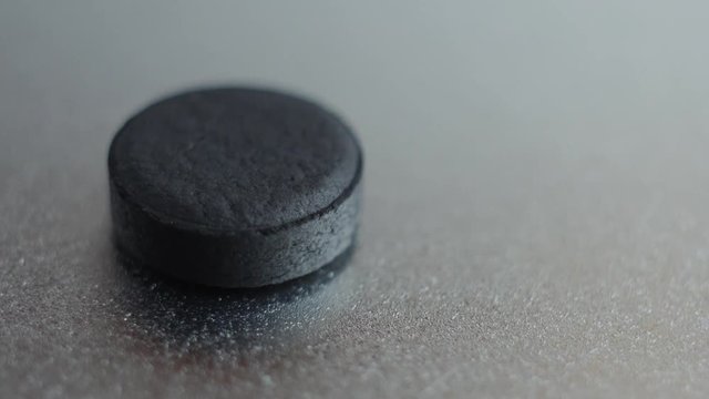 One activated coal tablet isolated on metallic background.