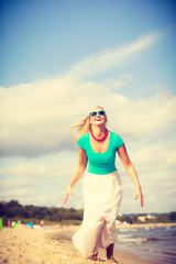 Blonde woman wearing dress playing jumping on beach