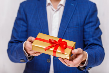 Male hands holding a gift box. Present wrapped with ribbon and bow. Christmas or birthday package. Man in suit and white shirt.