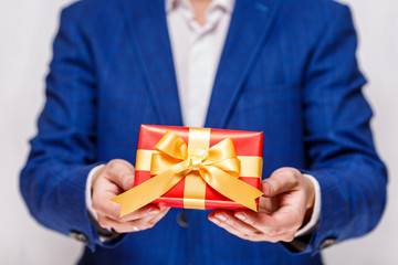 Male hands holding a gift box. Present wrapped with ribbon and bow. Christmas or birthday red package. Man in suit and white shirt.