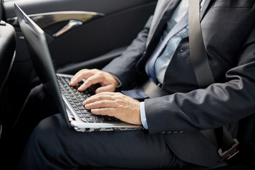 senior businessman with laptop driving in car