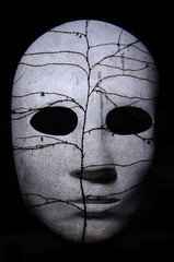 Textured mask with cracked rough wood  painted surface, neutral expression on dark background.
