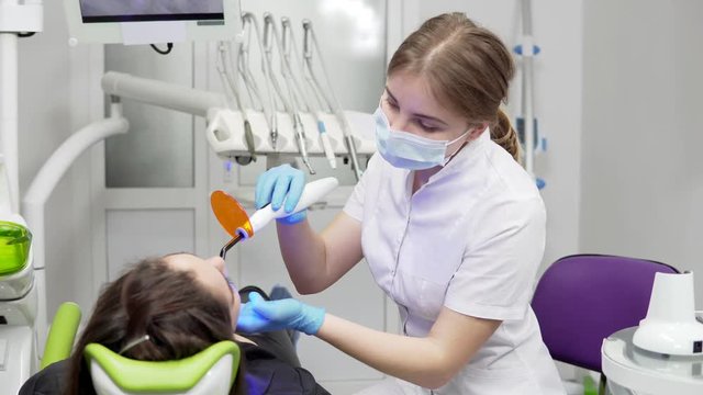 Young female dentist in mask and gloves using dental UV light equipment for polymer hardening