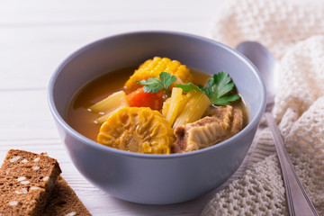 Puchero soup with corn and parsley on wooden table