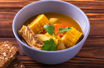 Puchero soup with corn and parsley on wooden table