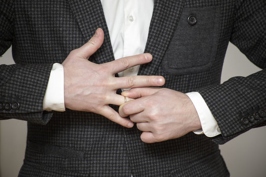 a man in a buttoned jacket struggling to remove wedding ring from his finger