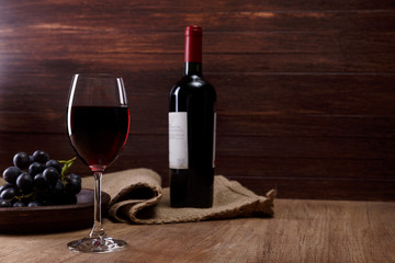 Red wine. Bottle with wineglass. Dark grapes branch on plate. On rustic wooden background.