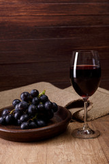 Red wine. Wineglass with dark grapes branch on plate. On rustic wooden background.