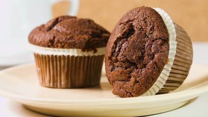 Two chocolate cupcakes on brown plate, one lying sideways