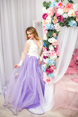 Young pretty woman in romantic negligee near bed decorated with flowers.