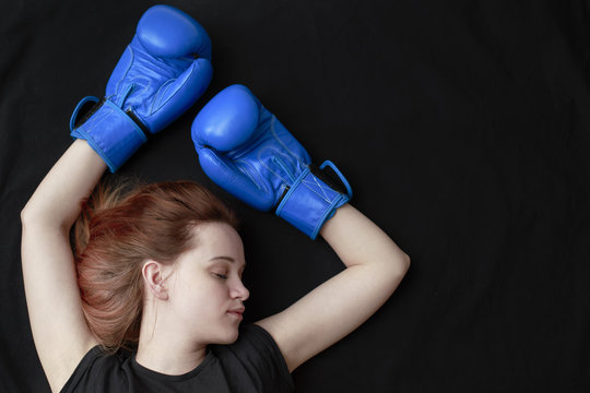 A girl in boxing gloves lies on the floor with her eyes closed in a knockout