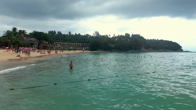 PHUKET, THAILAND - 20 JAN 2017: Many sunbeds are on sand beach and people swimming in the sea at cloudy day