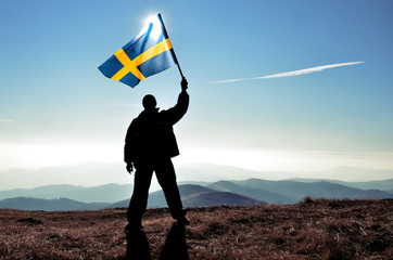 Successful silhouette man winner waving Sweden flag on top of the mountain peak