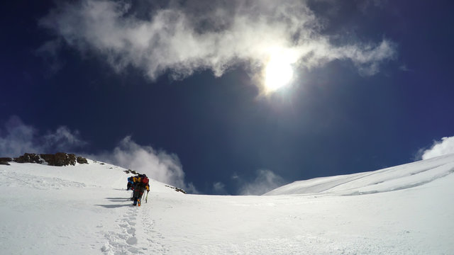 Mountaineer climbs snowfield on a sunny day high on a mountain