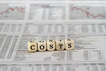 costs word built with letter cubes on newspaper background