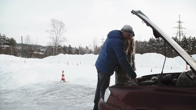 Driving instructor Talks about the engine of an open car hood to pretty teenage girl sitting in car