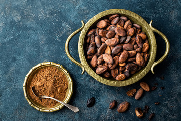 Cocoa beans and powder on dark background, top view, copy space, flat lay