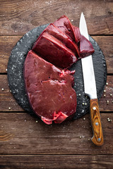 Raw liver on slate board on wooden background top view - obrazy, fototapety, plakaty