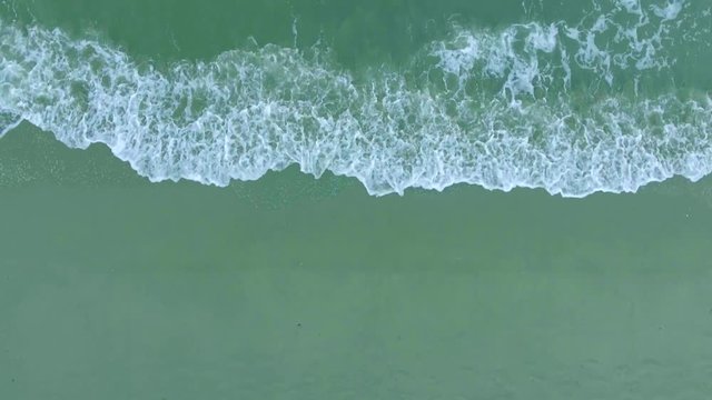 Top view foamy waves wash sandy beach aerial shot, shooting from helicopter, Camera moving from right to left