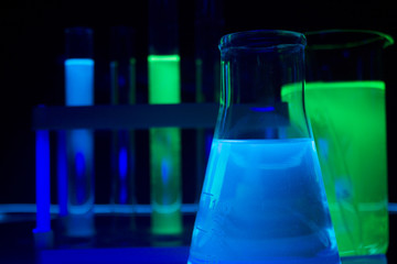 Photo composition of a laboratory bottles and test-tubes with glowing liquids standing on a glass...
