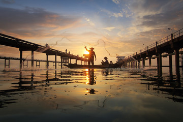 Fototapeta premium Silhouette of fishermen using nets to catch fish at the Bangpra lake with beautiful scenery of nature during sunrise time. Bang Pra Reservoir at Chonburi province in Thailand