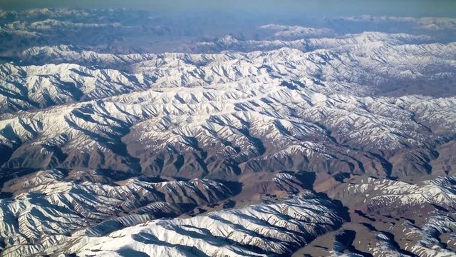 Slow flyover mountains southwest of Kabul, Afghanistan. Camera mounted to lighter-than-air ship (dirigible). Slow graceful pan over rugged landscape & caves where Taliban & Al-Qaeda terrorists hide.
